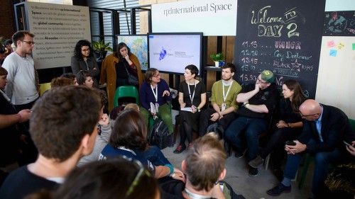 Visual Makerspace: Verschiedene Menschen sitzen in einem Kreis und unterhalten sich; darüber ein Schild „rp:international Space“