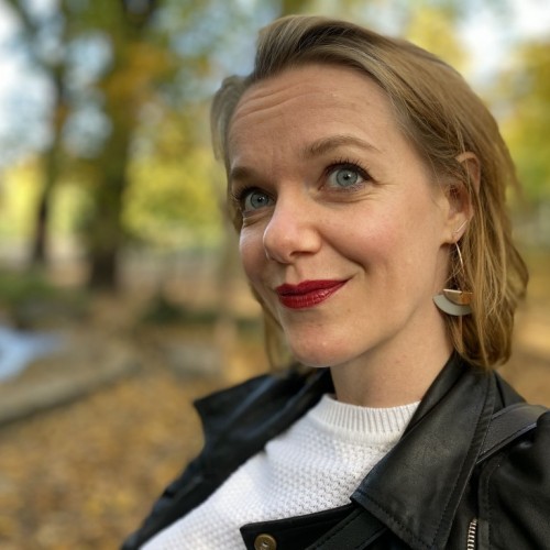 Picutre of Cathleen, outside, fall colours, short blond hair, red lips, white sweater, black leather jacket